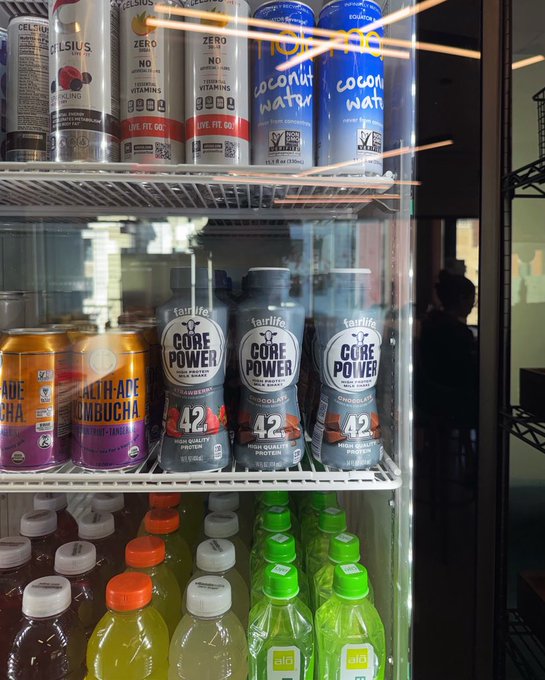 A refrigerated store shelf displays Celsius drinks, Core Power cans labeled “42,” kombucha cans, and rows of brightly colored bottled drinks.