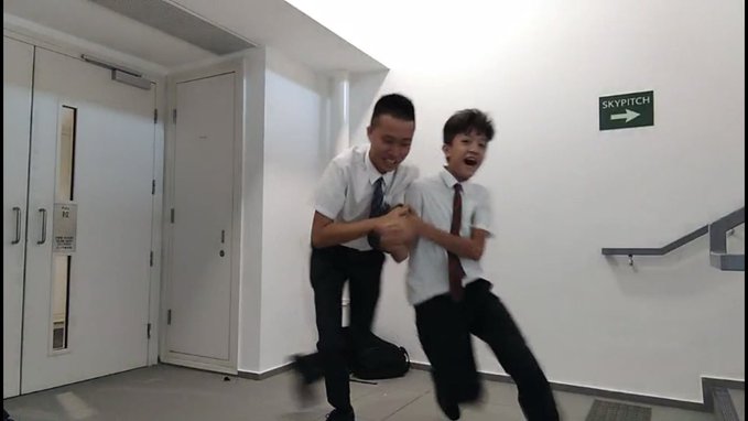 Two schoolboys in white shirts and ties playfully wrestle in a hallway near a sign reading "SKYPITCH" with a right arrow, one laughing as the other pretends to grab him—evoking the post's theme of two longtime middle school friends who can't be fooled by social engineering scams targeting their CEX contact.
