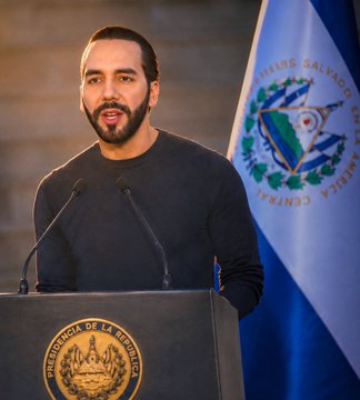 A photograph of Nayib Bukele, President of El Salvador, speaking at a podium bearing the country's seal.