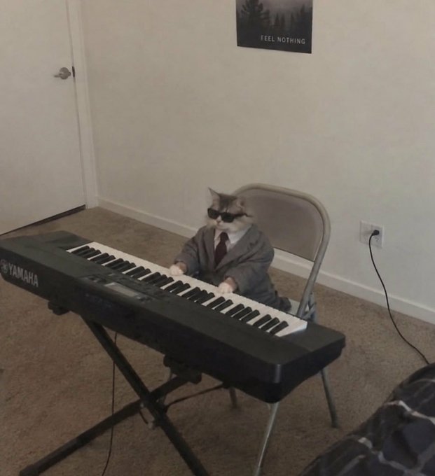 A photo of a cat wearing sunglasses and a gray suit with a red tie, sitting at a Yamaha keyboard piano in a room.