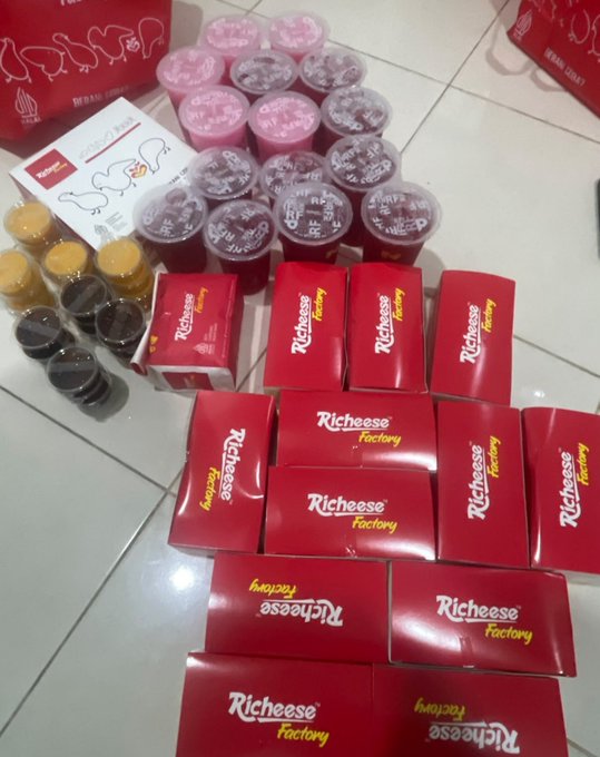 A photo showing a large haul of McDonald's food items on a tiled floor, including multiple red 'Richeese Factory' boxes, several McFlurry cups with Oreo toppings, drinks, and a paper bag.
