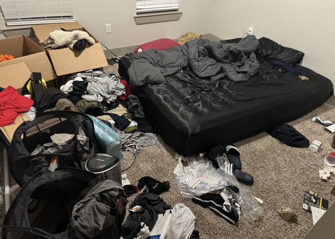 A very messy bedroom with an air mattress, scattered clothes, boxes, and various items strewn across the floor.