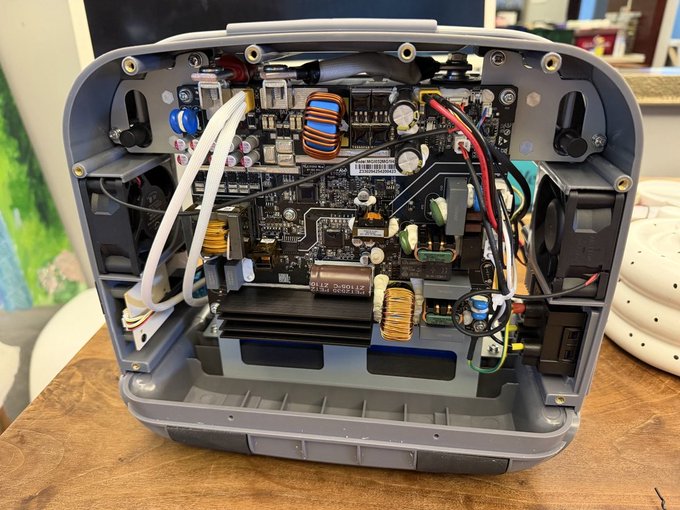 The internal components of an electronic device, likely a portable power station, showing a circuit board, wiring, cooling fans, and a large battery.