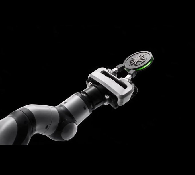 A close-up of a robotic arm's gripper against a black background, designed to hold a small circular component with green accents.