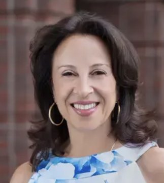 A smiling woman with shoulder-length brown hair, wearing hoop earrings and a blue and white floral top, poses in front of a brick wall, likely a headshot of candidate Hinojosa referenced in the post about the Texas Governor's race against Greg Abbott.