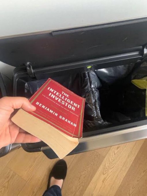 A hand throws Benjamin Graham's classic investment book "The Intelligent Investor" into a trash bin, humorously illustrating a post about a $SOL giveaway contest.