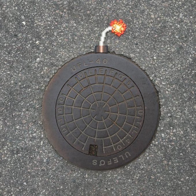 A circular black utility cover labeled "UFL-40 VALENCIA UTILITY" and "U1010410" is embedded in asphalt, with a small orange-and-white marker flag protruding from a pipe at its top.