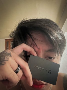 A young person with dark hair holds a sleek black Tangem card close to the camera, partially obscuring their face. The Tangem logo is visible on the card, connecting with the post's excitement about receiving a new Tangem ring for review.