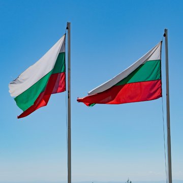 Two flags of Bulgaria, featuring horizontal white, green, and red stripes, waving on flagpoles against a clear blue sky.