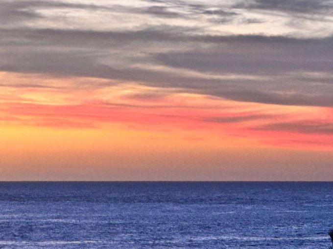 A serene sunset view over the ocean, with orange and pink hues blending into a cloudy sky.
