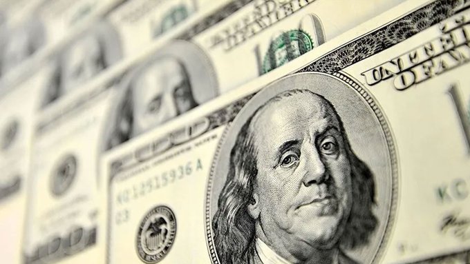 A close-up photograph of multiple overlapping U.S. one hundred dollar bills, with Benjamin Franklin's portrait prominently featured on the foreground bill.