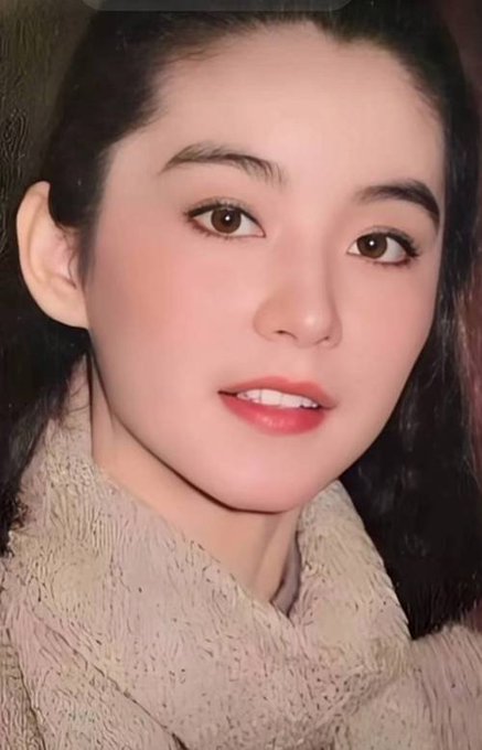 A close-up portrait of a young woman with dark hair, defined eyebrows, and red lipstick, wearing a fuzzy beige sweater.