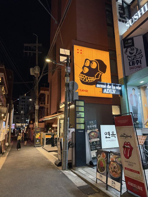 A nighttime street scene in Korea featuring restaurants including 'acmé de la vie ADLV' and '대취 DAECHWI' with various Korean signs and menu displays.