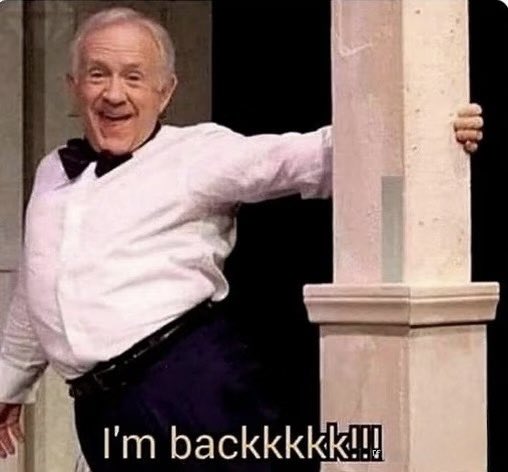 The image features an older man wearing a white shirt, black bowtie, and pants standing next to a tall column with his arm outstretched. Below him, there's text that reads "I'm backk...!". The context of this image is unclear without additional information about what it represents or the background behind the man.