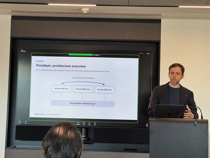 A man presenting at a podium next to a screen showing a slide titled 'Prividium: architecture overview' detailing private EVM zones connected to a neutral public settlement layer.