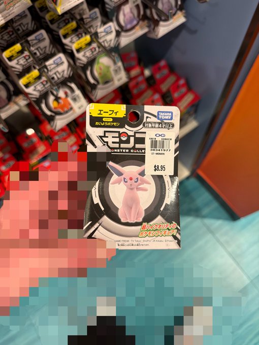 A hand holding a Pokémon trading card featuring Espeon (エーフィ) priced at $8.95, with Japanese text and the 'MONSTER COLLE' branding, set against a blurred display of similar cards.