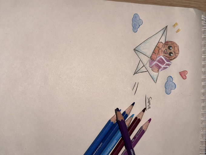 A hand-drawn colored pencil illustration in a spiral notebook showing Baby Yoda (Grogu) in a paper airplane with clouds and rainbows, labeled 'Santa', with colored pencils resting on the page.