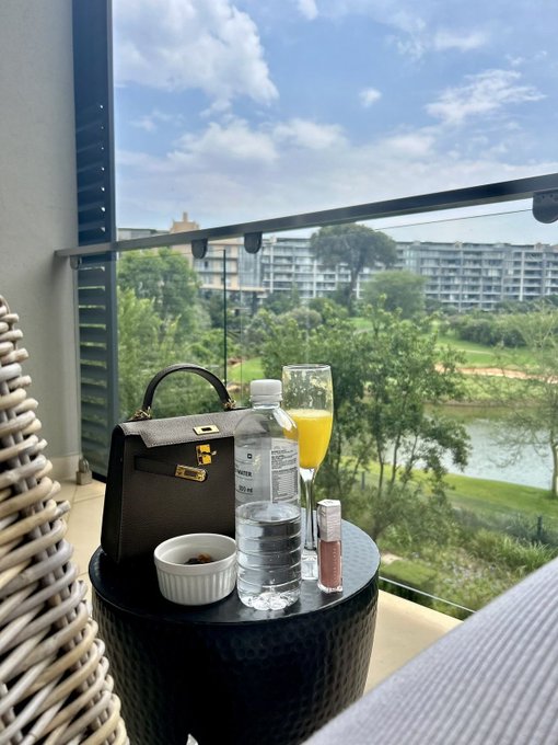 The image shows an outdoor scene with a black table holding various items such as a water bottle, wine glass, handbag, bowl of food, and a small white dish. The table also has a purse placed next to it. In the background, there is a balcony overlooking a lake or river, providing a serene view for relaxation. The image includes text that reads "Good afternoon While most projects focus on today's challenges, @quipnetwork is building for the future secured by post-quantum infrastructure." This suggests that the person who set up this scene might be interested in investing in new technologies and innovations to secure their future or be intrigued by the concept of a post-quantum world.
