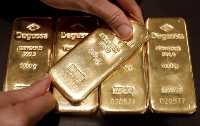A close-up of several Degussa 999.9 fine gold bars, each weighing 1000g, with one being held by a hand.