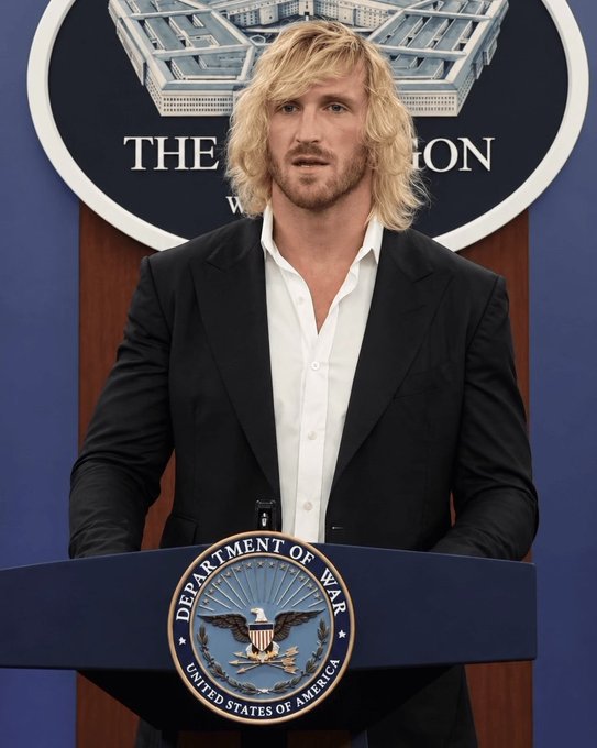 A blonde man in a black suit and white shirt stands at a podium bearing the 'Department of War, United States of America' seal, with 'THE PENTAGON' visible on the seal behind him.