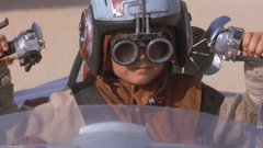 The image features a young boy wearing a helmet with goggles, sitting inside a car. He appears to be driving or playing with toy cars, as he holds two toy steering wheels in his hands. The background of the image is blurred, drawing attention to the main subject and emphasizing him as the focal point.