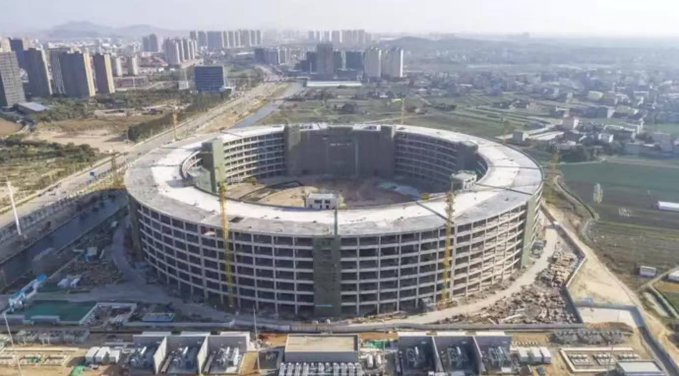 An aerial view shows a massive circular building under construction, surrounded by construction equipment and a developing urban landscape. This represents the transformation of traditional mining infrastructure into massive AI data centers, as the crypto mining industry pivots toward AI computing facilities amid shifting demand.