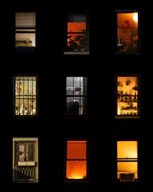 A grid of nine windows at night showing various scenes such as plants, a bathtub with bubbles, sunset views, and silhouettes of people inside.