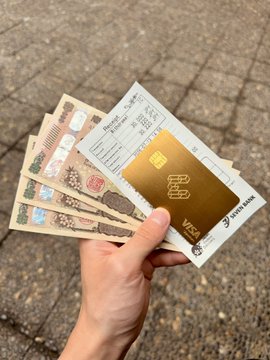 A hand holds Japanese yen banknotes and receipts alongside a gold EtherFi Visa card on a paved surface, illustrating the low ~1.5% FX fee the user experienced when withdrawing cash from a Japanese ATM with their EtherFi card.