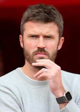 A man with a beard and short brown hair, wearing a light gray sweater and a black smartwatch, rests his hand thoughtfully against his chin while wearing a ring on his finger. The image likely depicts a manager or coach showing a contemplative or frustrated expression following Manchester United's draw against 18th-placed Tottenham at Old Trafford.