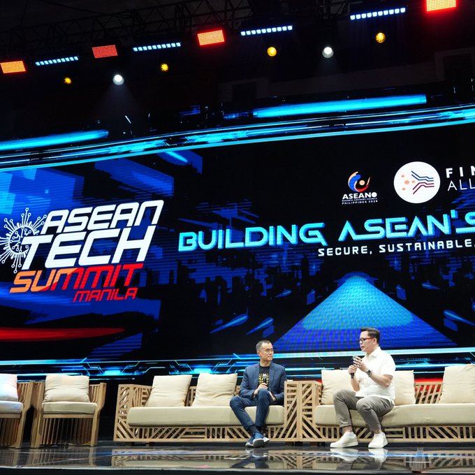 Two men seated on a stage on a sofa at the 'ASEAN TECH SUMMIT MANILA' event, with a large screen behind them displaying 'BUILDING ASEAN'S SECURE, SUSTAINABLE' future.