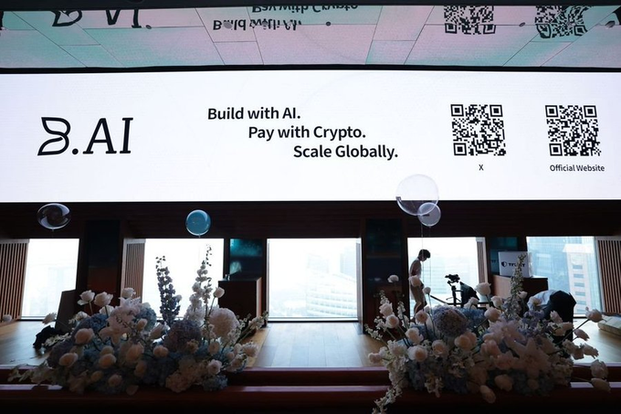 A large illuminated sign reads 'B.AI Build with AI. Pay with Crypto. Scale Globally.' with two QR codes, displayed above floral arrangements in an indoor venue.