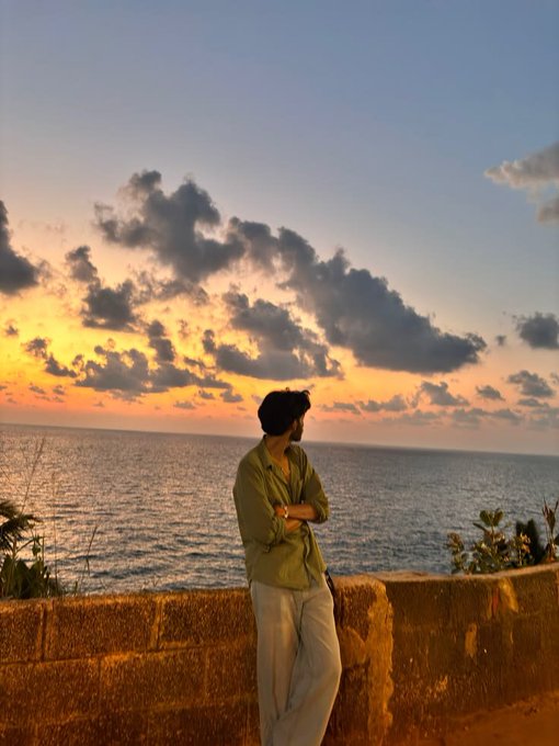 A man in a green shirt and light pants stands at a stone wall overlooking the ocean during a vivid sunset, gazing out at the horizon. The image reflects a contemplative, forward-looking mood that complements the post's discussion of Smart Vault's hands-off approach to managing assets, where users can step back while capital is allocated across DeFi and CeDeFi strategies.