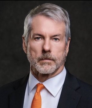 A professional headshot of a distinguished-looking man with gray hair and a beard, wearing a dark suit with an orange tie, likely depicting Michael Saylor. The image relates to the post by visually representing the executive behind Strategy (formerly MicroStrategy) as the context highlights his bold statement about the company's plans to continue accumulating Bitcoin.