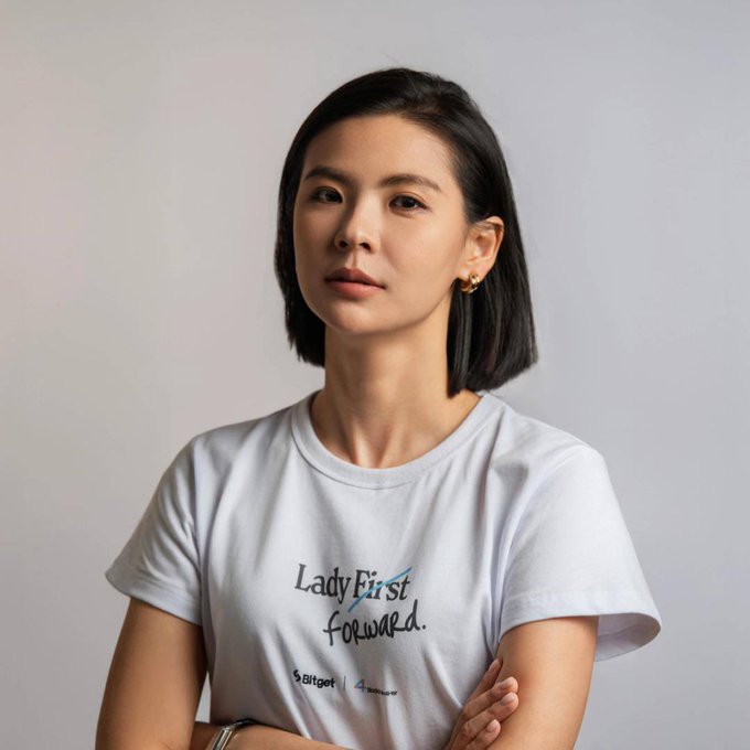 A portrait of a young Asian woman with shoulder-length dark hair wearing a white t-shirt with the text 'Lady First Forward' printed on it, posing against a light gray background with arms crossed.