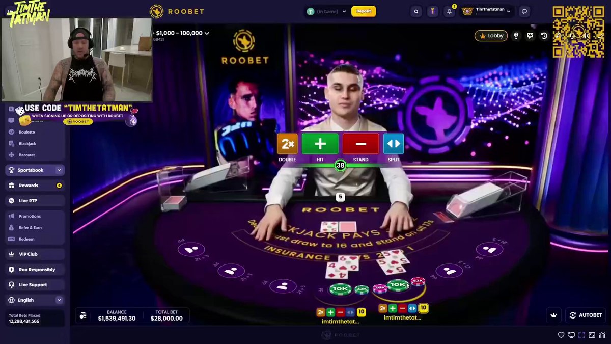The image shows a person playing blackjack at a table, with a large purple screen displaying the game's interface. The player is wearing a white shirt and holding a deck of cards. There are two decks visible on the table, one near the center and another towards the right side. A man can be seen in the background, possibly observing or waiting for his turn to play. The post about Roobet Blackjack was shared by someone who hit 190K on the game, indicating that it is a popular and well-liked casino game among players.