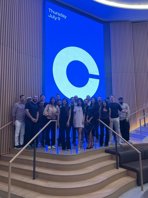 A group photo of the agenticscredit team and attendees posing on a staircase at an event, with a large "C" logo and "Thursday July 9" displayed on a screen behind them, complementing the post about their choice of the Base network for their perpetual futures-based credit system.