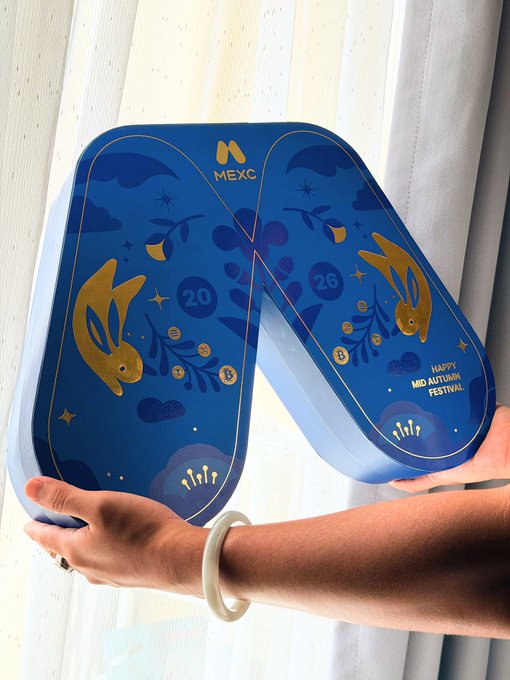 A person wearing a jade bracelet holds up a blue tin shaped like the number "20" and "26," featuring the MEXC logo, gold rabbits, and text reading "Happy Mid Autumn Festival." The decorative packaging reflects the post's theme, serving as a thoughtful Mid-Autumn Festival gift from MEXC to its community.