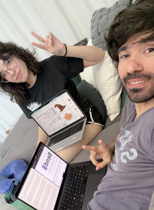 A selfie of a young woman with curly hair and glasses making a peace sign, and a young man, sitting on a couch with two laptops on their laps displaying websites including bnbg.