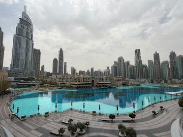 An aerial cityscape showing a turquoise pool area in the foreground surrounded by dense skyscrapers under an overcast sky.