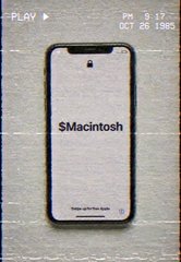 A smartphone screen displaying the text 'SMacintosh' against a beige background with 'PLAY', 'Fri 5:17 PM', and 'OCT 26, 1985' shown in a vintage interface style.