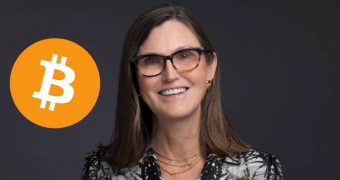 A smiling woman with brown hair and glasses appears next to an orange Bitcoin logo, representing Cathie Wood of ARK Invest, who is shown here alongside the cryptocurrency she projects could reach a $1.5 million target by 2030.