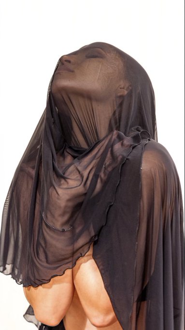 A person draped in a sheer, flowing black fabric covering their head and body, photographed against a plain white background.