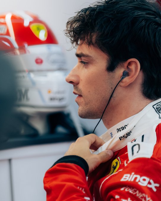 Charles Leclerc, wearing his red Ferrari team gear with visible "BingX" and "PERON" sponsor logos, listens intently with earbuds in, with his iconic red and white racing helmet displayed behind him. The image captures the focused, composed demeanor of the F1 driver following his remarkable P22-to-P4 comeback, perfectly complementing the post's celebration of his performance ahead of the Token2049 after-party appearance.