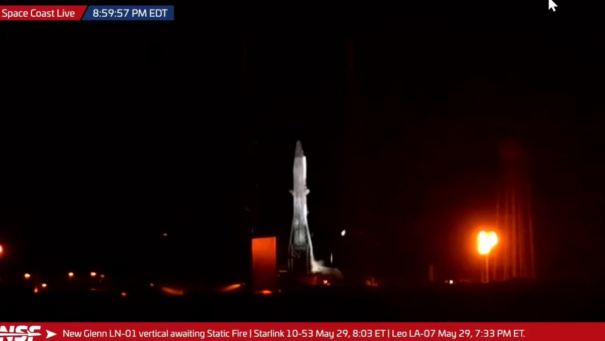 The image shows a rocket launch taking place at night, with the rocket being lit up against the dark sky. A red banner can be seen in the background, possibly indicating an event or promotion related to the rocket launch. The caption of the image reads "My tokens the moment I hit the buy button." This suggests that the viewer is likely a fan who has purchased tickets for this rocket launch and is excitedly watching it unfold on their computer screen.