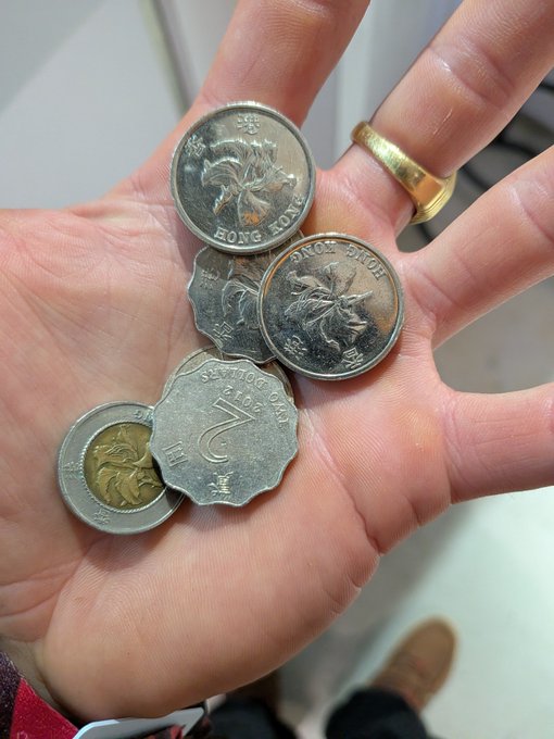 A person's open palm displays several Hong Kong coins, including a distinctive seven-sided $2 coin with "SEVEN DOLLARS CLUB COIN" inscription and "HONG KONG" text, alongside round $5 and $10 denominations. The caption humorously contrasts the worn, jingled loose change with the post's declaration that the items are "going fail," playing on the coins' rough, weathered appearance.