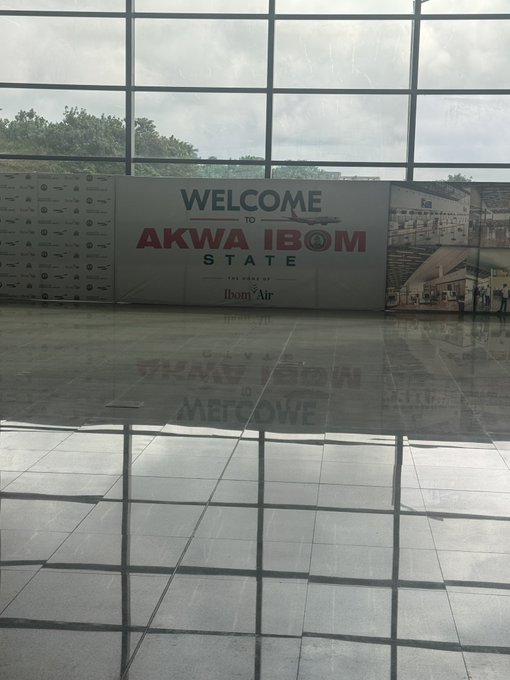 A welcome sign inside an airport or terminal that reads 'WELCOME TO AKWA IBOM STATE' with 'Ibibom Air' logo, reflected on the polished tile floor in front of large glass windows.