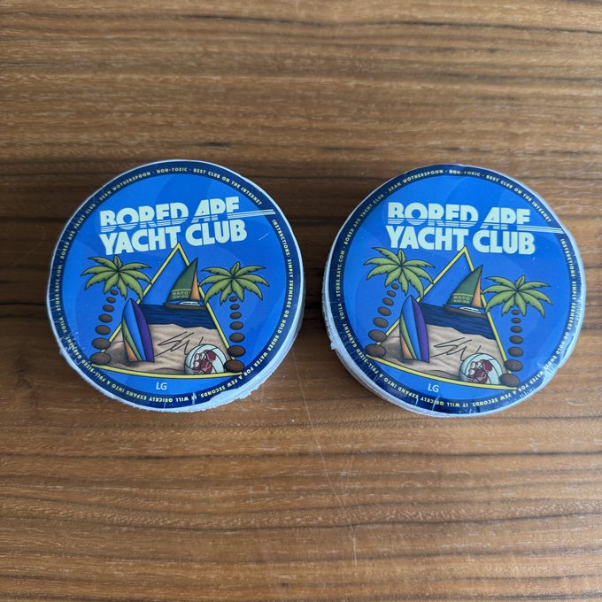 Two blue circular tins of 'Bored Ape Yacht Club' branded cannabis products labeled 'Sour Diesel' sit on a wooden surface.