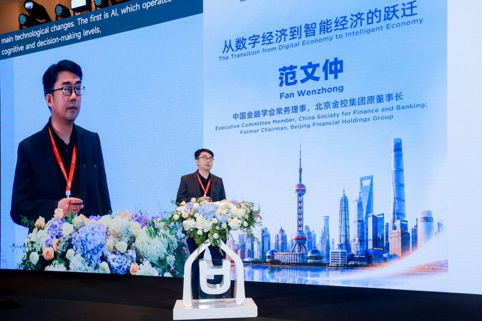 A man speaks at a podium during a conference with a backdrop titled '从数字经济到智能经济的跃迁 / The Transition from Digital Economy to Intelligent Economy', introducing speaker '范文仲 / Fan Wenzhong', Executive Committee Member of China Society for Finance and Banking.