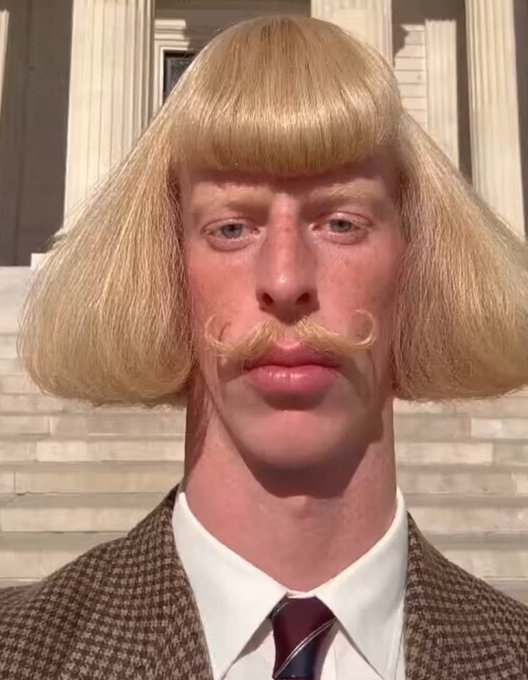 A digital caricature featuring a person with exaggerated facial features, a blonde bowl-cut wig, and a curled mustache, wearing a brown tweed jacket, white shirt, and striped tie.