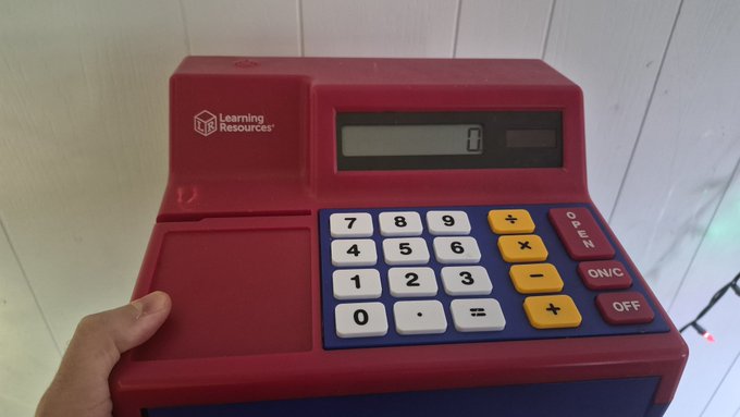 A child's toy cash register from Learning Resources, featuring a red body, blue panel, white number keys, and yellow function buttons.